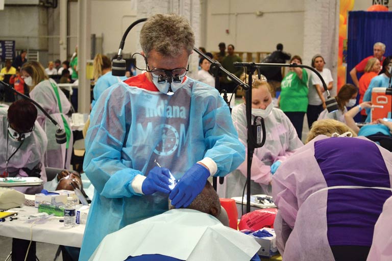 People wearing face masks and holding dental tools stand over patients.