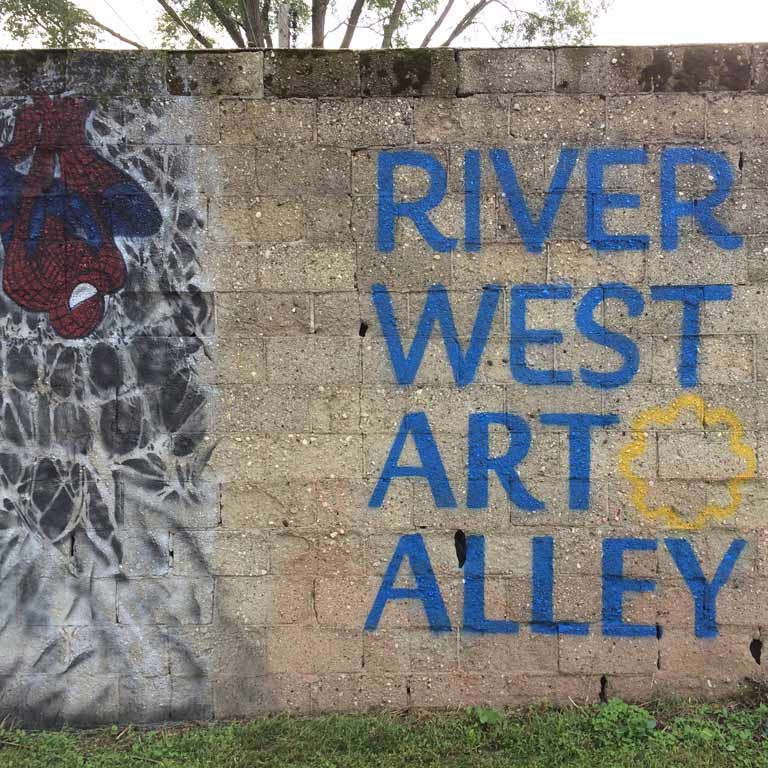 A concrete outdoor wall with the words River West Art Alley painted on it.
