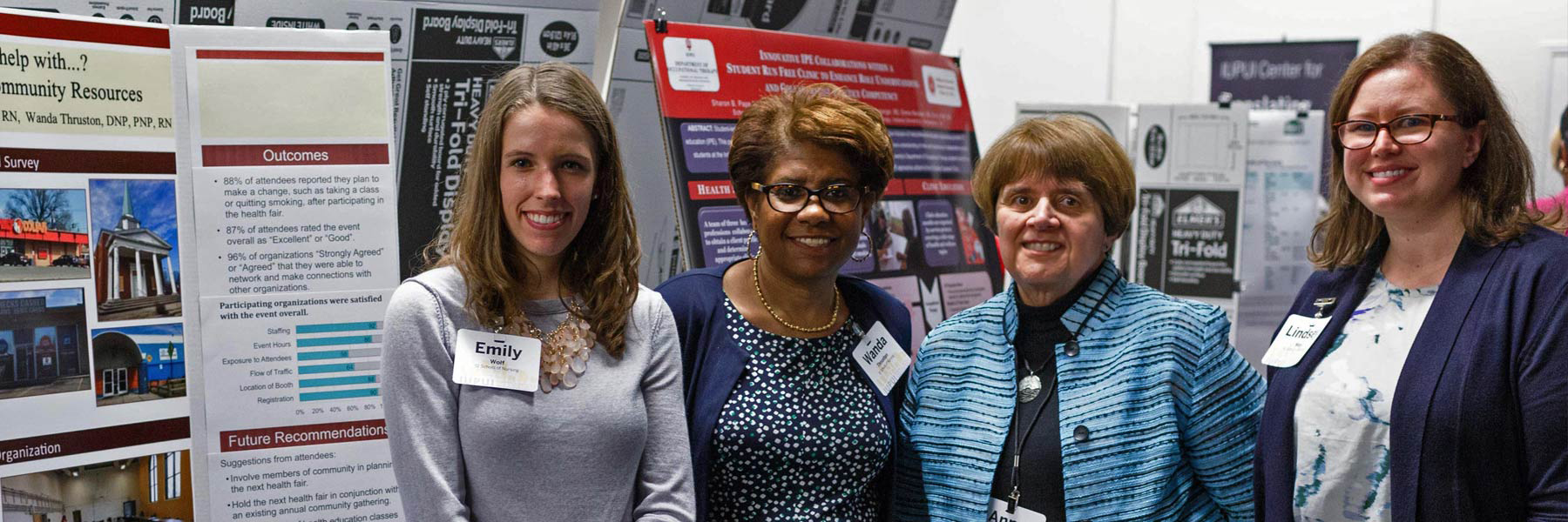 Four women stand smiling in front of research posters.